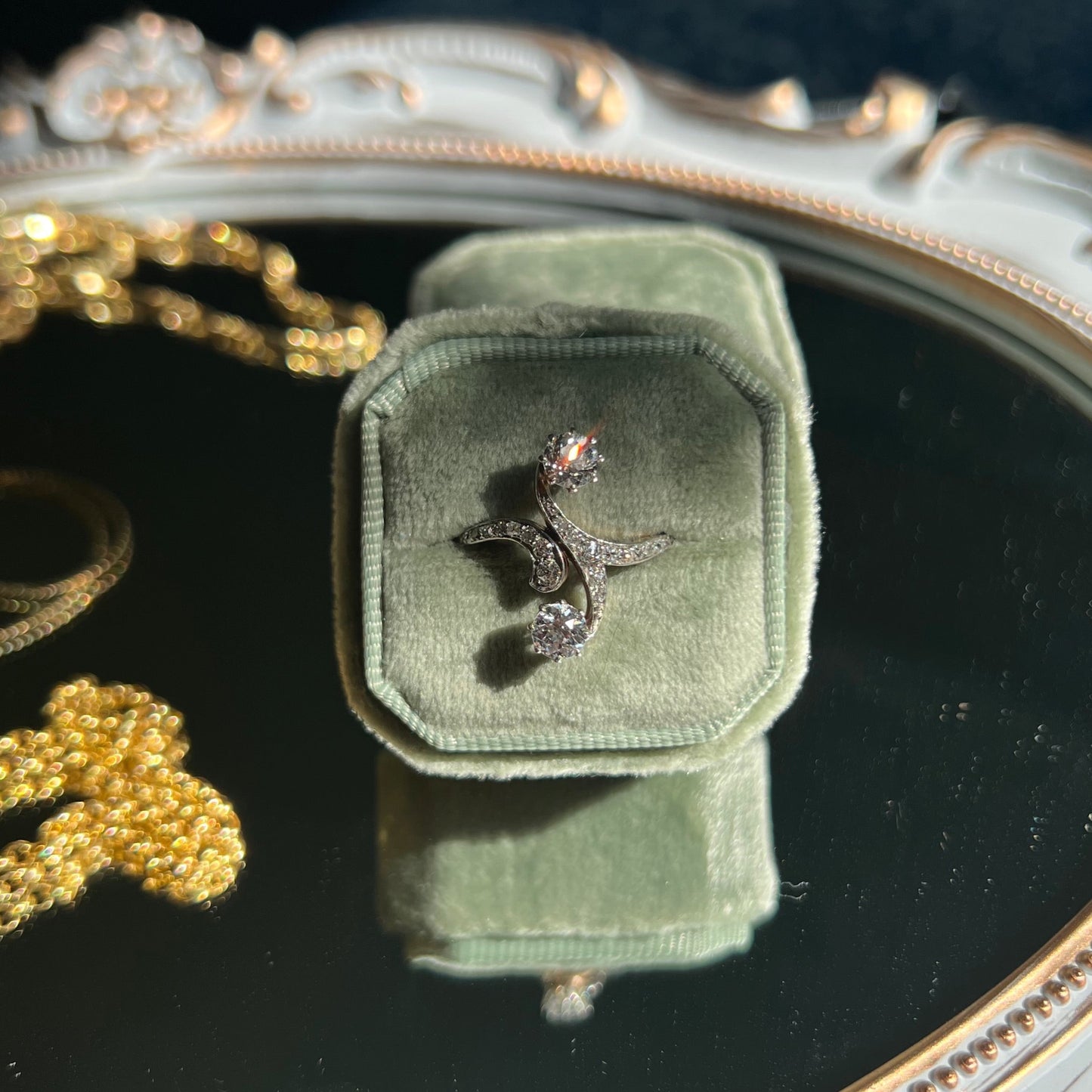 moi et toi two stone diamond ring with curved diamond band in a light green ring box on top of a mirror