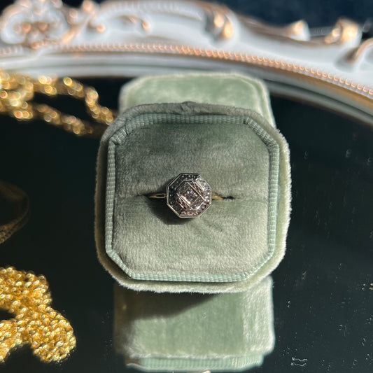 octagon shaped gold ring with diamond center in a light green ring box on top of a mirror