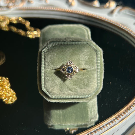 kite shape filigree sapphire ring in a light green ring box on top of a mirror