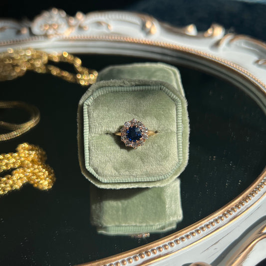 sapphire with diamond halo ring in a light green ring box on top of a mirror